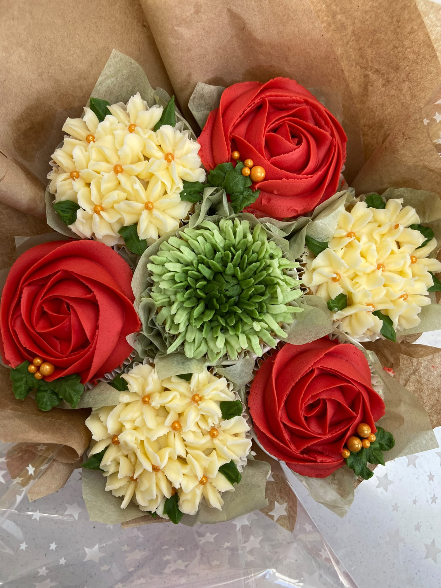 Classic Christmas Bouquet cupcake bouquet with red poinsettia, cream rose, sage chrysanthemum, holly and pinecone buttercream cupcakes wrapped in kraft paper with a sage ribbon bow