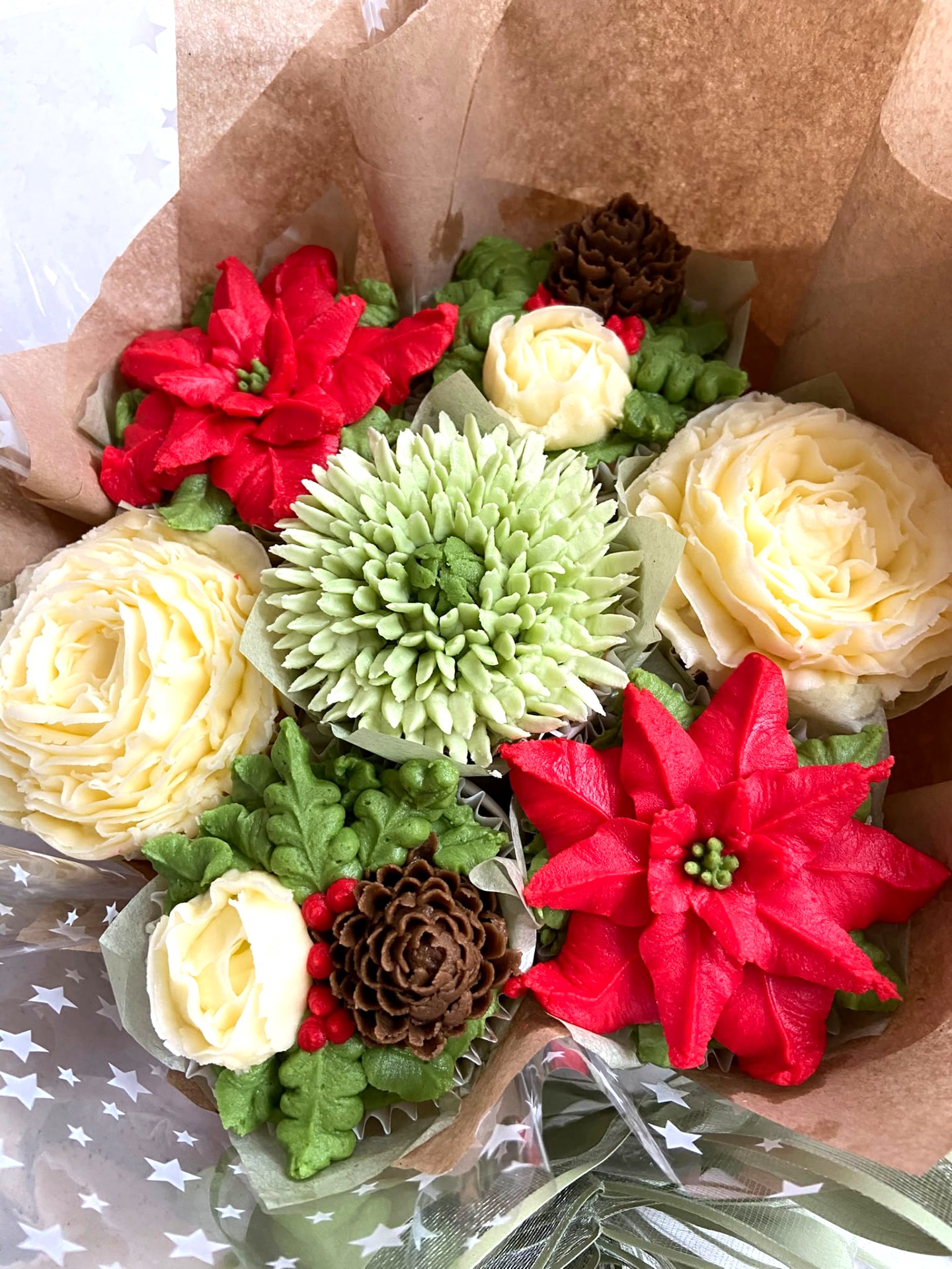 Christmas Blooms seasonal cupcake bouquet with red poinsettia, cream rose, sage green and pinecone buttercream cupcakes, wrapped in kraft paper and star-print wrap
